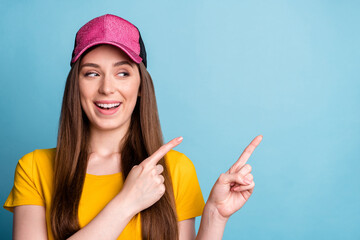 Photo of curious lady indicate forefingers empty space look side wear pink cap yellow t-shirt isolated blue color background