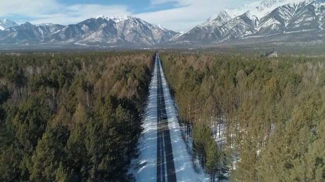 Drone forward amazing snow-capped mountains Arshan Buryatia, straight asphalt highway road to Tunki nature reserve. Winter spruce pine forest. Lonely car is driving. Adventure travel to Baikal region