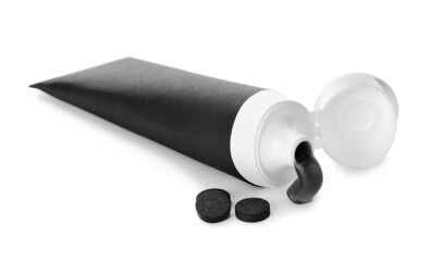 Tube with black toothpaste and activated carbon pills on white background