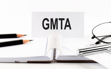 Text GMTA on paper card,pen, pencils, glasses,financial documentation on table - business concept