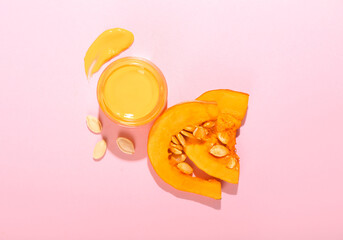 Jar of natural mask and slices of pumpkin on pink background