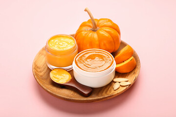 Plate with jars of natural mask and pumpkin on pink background
