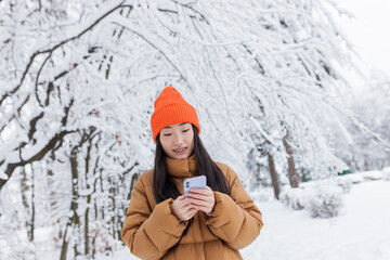 Beautiful Japanese teenager walks in the winter park uses the phone shopping online in the store on...