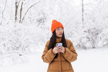 Young Asian woman, in the park on a date, waiting, on a winter snowy day, online uses the phone