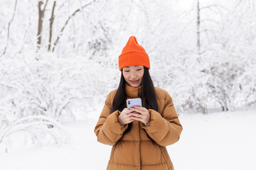 Young Asian woman, in the park on a date, waiting, on a winter snowy day, online uses the phone