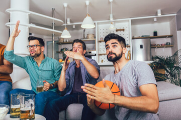 Happy friends or basketball fans watching basketball game on tv and celebrating victory at home.