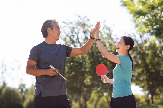 Happy mature couple playing table tennis outdoors