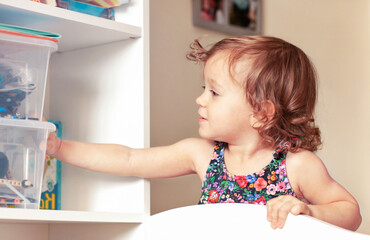 a little girl is  reaching into the closet for toys