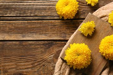 Fototapeta na wymiar Board with yellow chrysanthemum flowers on wooden background