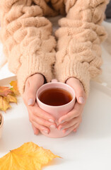 Woman with cup of hot tea at white table on autumn day, closeup