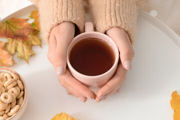 Woman with cup of hot tea at white table on autumn day, closeup