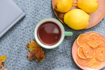 Green cup of hot tea and fallen leaf and food on grey fabric background
