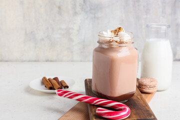Mason jar of tasty coffee with cinnamon and candy cane on light background