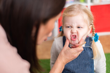 Woman speech therapist helps cute girl to learn correct pronunciation and literate speech