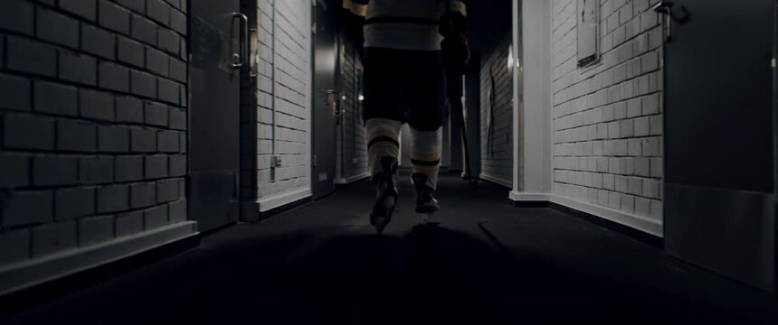 HANDHELD TRACKING Ice hockey player walking alone through the dark hallway towards rink. Shot with 2x anamorphic lens
