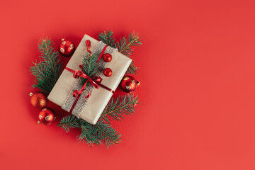 Craft gift box with spruce branch and christmas ornaments on a red background. Holiday concept.