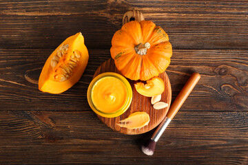 Board with jar of natural mask, pumpkins and makeup brush on wooden background