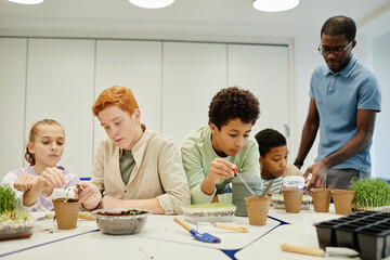 Diverse group of kids planting seeds while experimenting at biology class in school