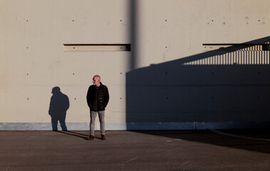 Full length of adult man in winter clothes standing against white wall with sunlight and shadow