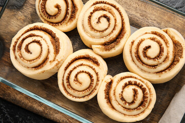 Baking dish with uncooked cinnamon rolls and on black background, closeup
