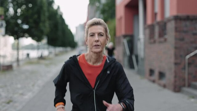 Active aged woman in sport clothes jogging alone on street