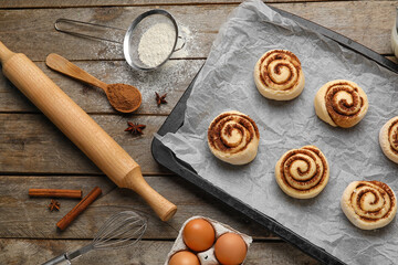 Fototapeta na wymiar Baking dish with uncooked cinnamon rolls and ingredients on wooden background, closeup