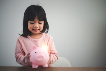 Little Asian girl saving money in a piggy bank, learning about saving, Kid save money for future education. Money, finances, insurance, and people concept