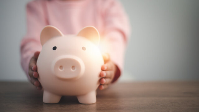 Little Asian girl saving money in a piggy bank, learning about saving, Kid save money for future education. Money, finances, insurance, and people concept