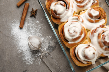 Baking dish of tasty cinnamon rolls with cream on grey background, closeup
