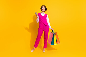 Photo of dreamy sweet young woman dressed pink suit holding shoppers modern gadget looking empty space isolated yellow color background