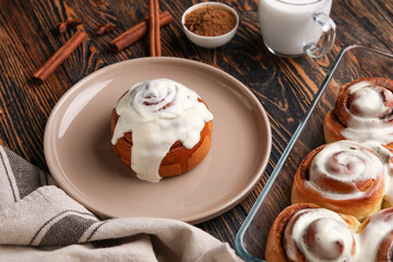 Plate and baking dish with tasty cinnamon rolls on wooden background