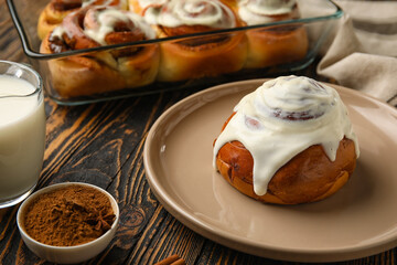 Plate of tasty cinnamon roll with cream on wooden background