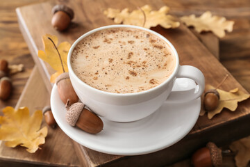 Cup of coffee with acorns and autumn leaves on wooden background