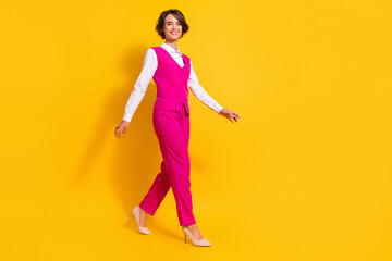 Full size photo of optimistic young brunette lady go wear pink suit stilettos isolated on yellow background