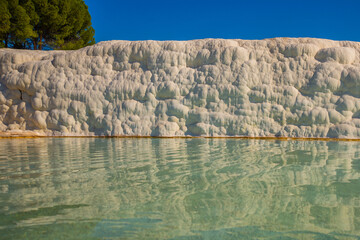 PAMUKKALE, TURKEY: White travertines and a pool with clear water in Pamukkale on a sunny day.