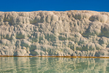 Fototapeta na wymiar PAMUKKALE, TURKEY: White travertines and a pool with clear water in Pamukkale on a sunny day.