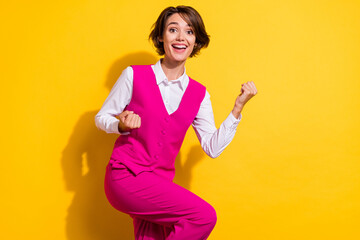 Photo of pretty lucky young woman dressed pink suit rising fists empty space smiling isolated yellow color background