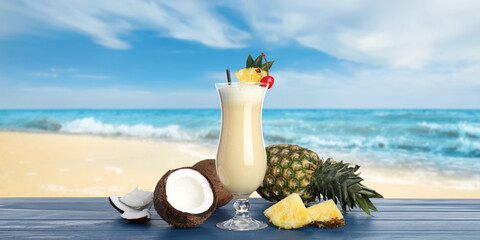 Tasty Pina Colada cocktail on blue wooden table near ocean. Banner design