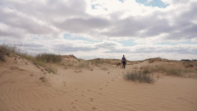 Female hiker with a dog walking through sandy desert dunes