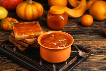 Bowl of sweet pumpkin jam with toasts on wooden background