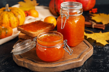 Jars of sweet pumpkin jam and toasts on black background
