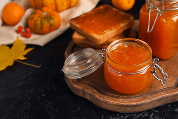 Jars of sweet pumpkin jam and toasts on black background