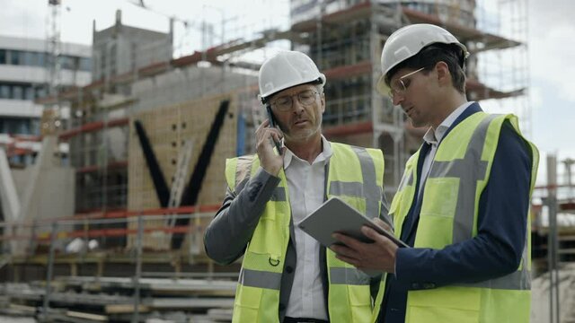 Male engineers using mobile and tablet on construction site