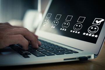 Close up image of finger pressing face emoticon on the laptop and selecting smiley face icon and a 5 star rating. Demonstrates that customer satisfaction is essential to a successful business.