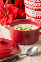 Top view of leek cream with almonds and chives in little red casserole, on white table with spoon, in vertical