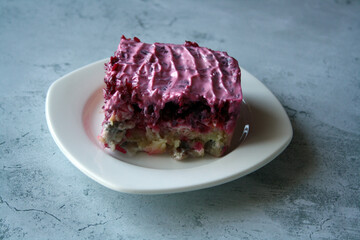 Layered salad of herring, potatoes and beets with mayonnaise in a white plate.