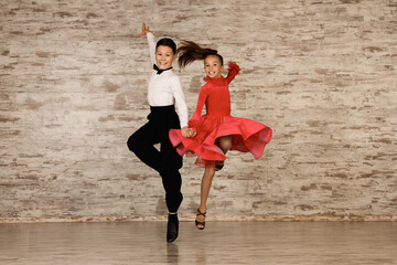 Beautifully dressed couple of kids dancing together in studio - obrazy, fototapety, plakaty