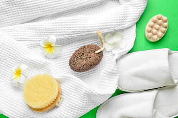 Bath supplies for foot massage with bathrobe and slippers on green background, closeup