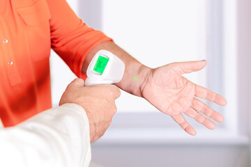 Obraz premium The physician monitors the patient's temperature at the wrist with a pistol body thermometer. Prevention of covid and omicron virus disease by measuring fever