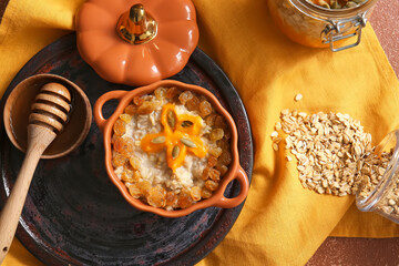 Pot of tasty oatmeal with pumpkin and raisin on table